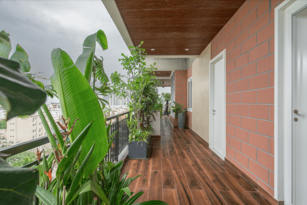 Long balcony corridor design with exposed brick wall and tropical plants in Pune