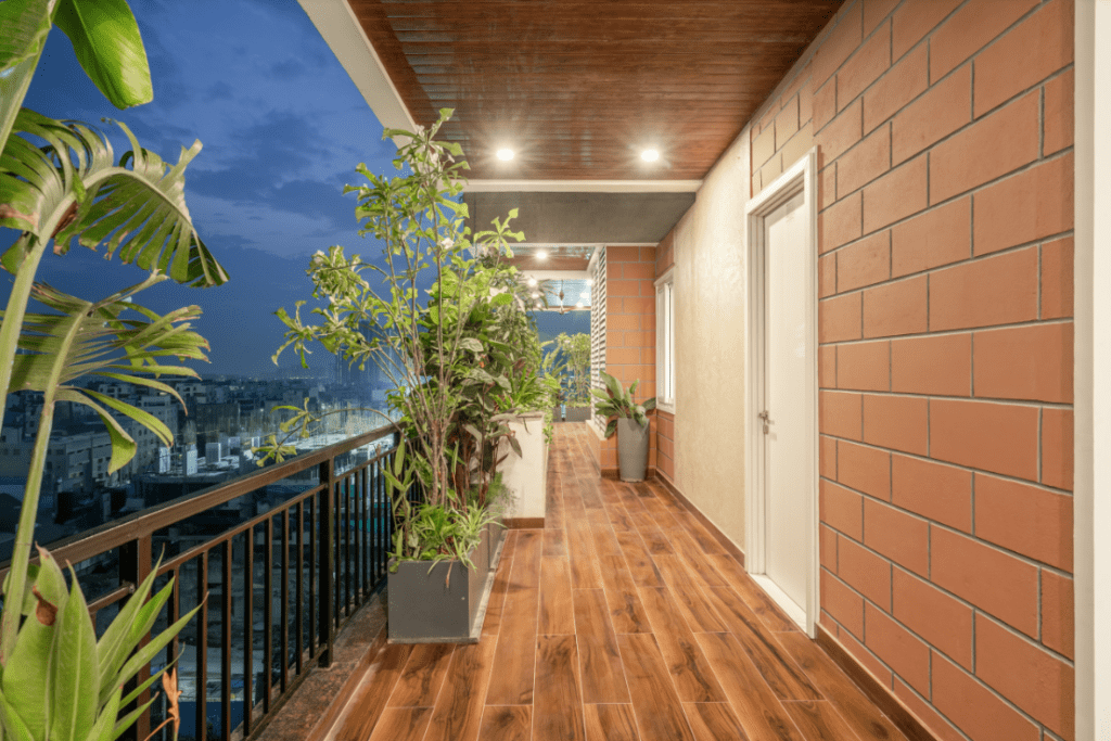 Balcony garden design with wooden flooring, exposed brick wall, and city view in Pune