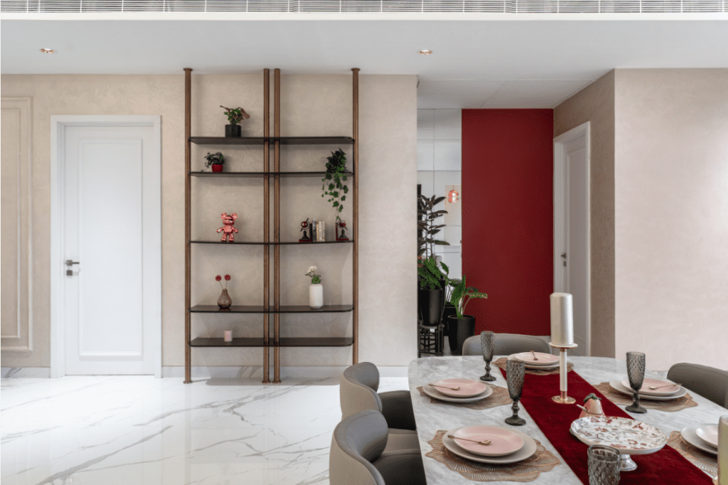 Dining room with decorative open shelving partition and maroon accent wall interior design in Pune